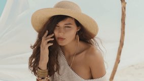 A romantic boho-style fashion model wearing a straw hat and flowy white dress, posing elegantly on a sunny beach. Soft, serene, and stylish footage showcasing bohemian beauty. - Powered by Shutterstock - Get 15% off with code: PIKWIZARD15