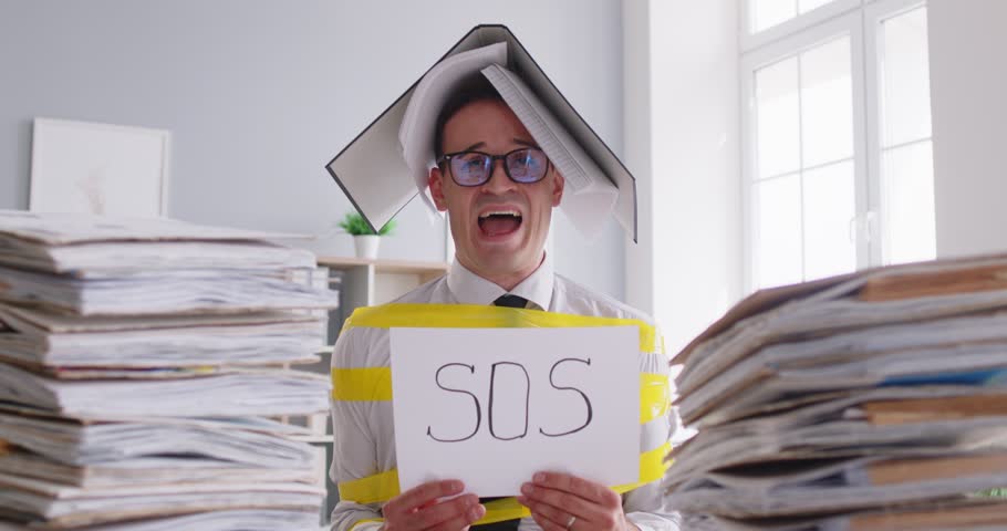Exhausted businessman screaming and holds an SOS sign while working with documents in the office. He shows signs of fatigue and overwork, struggling with business problems and paperwork.