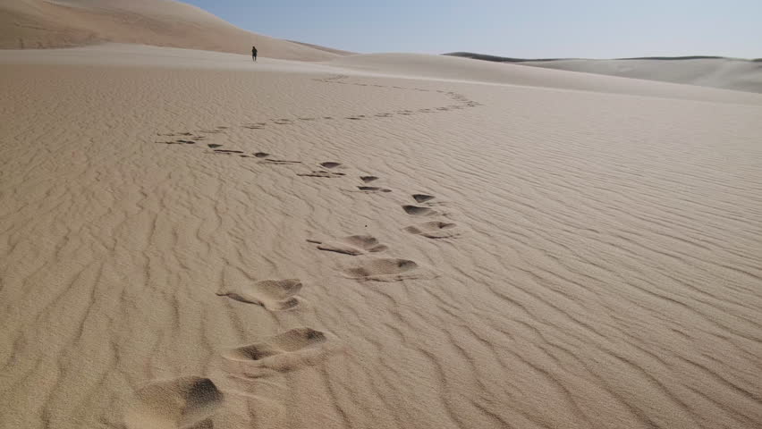 Man walking alone in a sand dunes. Footprints in a desert. Sahara desert near Siwa oasis in Egypt. Handheld real-time footage