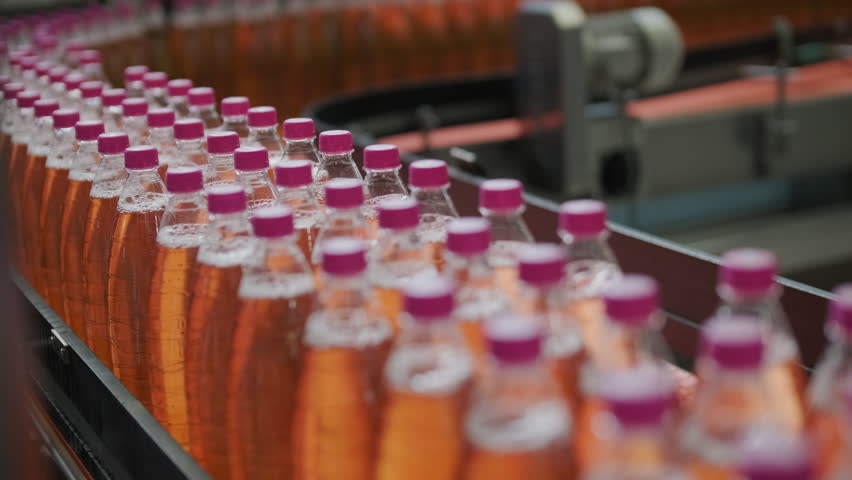 Automated production line for bottling water or juice in a modern beverage factory. Plastic bottles move on conveyor belts through filling, capping, and packaging stages in industrial setting.