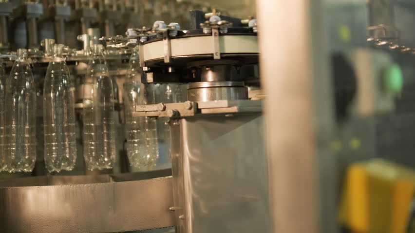 Automated production line for bottling water or juice in a modern beverage factory. Plastic bottles move on conveyor belts through filling, capping, and packaging stages in industrial setting.