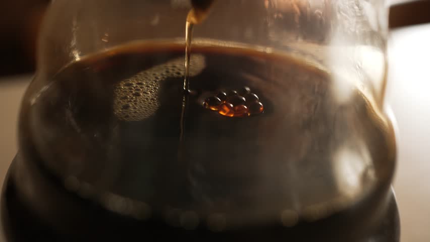 Golden coffee streaming through filter, cascading into glass pot with foaming liquid and bubbles developing on dark surface, capturing morning brewing ritual