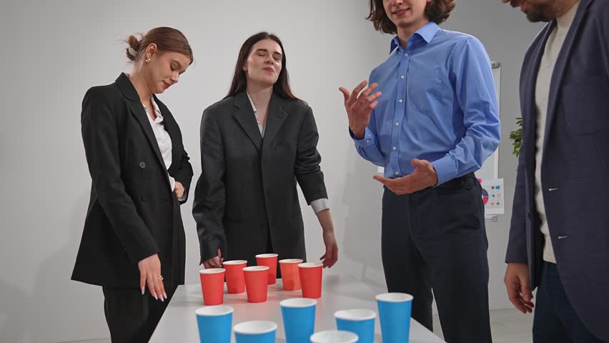 A group of professionals is focused on winning a team building game in an office setting, using red cups.