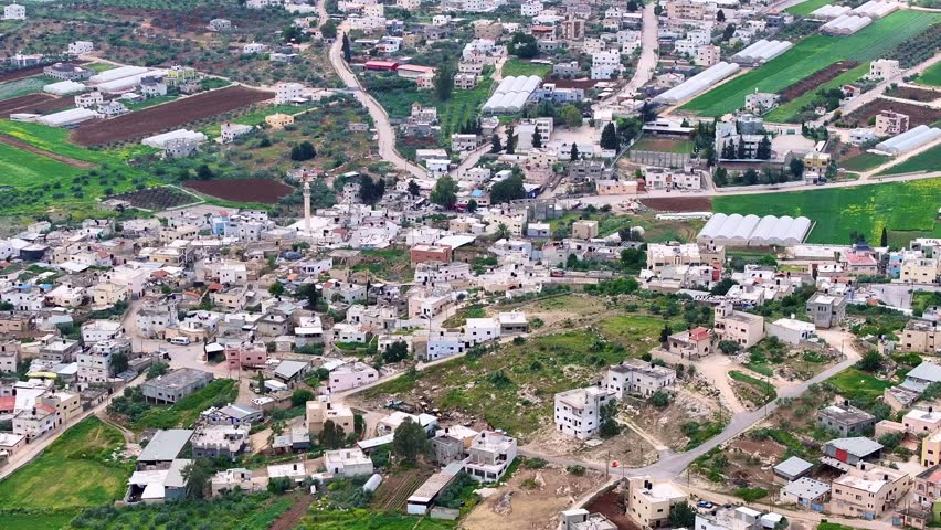 Aerial footage of a  hillside Arab village in Israel with dense cluster of flat-roof homes, winding roads, and natural mountainous terrain.  view showcases Middle Eastern Arab living in Israel .