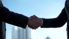 Confident business professionals closing partnership deal firm handshake. Against window in office, agree to deal or say hello. Urban skyline revealing corporate environment and collaborative success - Powered by Shutterstock - Get 15% off with code: PIKWIZARD15