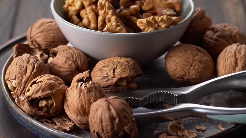 Plate of walnuts and bowl of walnut halves with nutcracker tool rotation