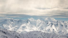 Winter mountains in snowy timelapse. Snow-capped mountain ranges on cloudy day. Whole sky is in pearl clouds rays of sun are about beautiful glare on snow, breaking through clouds. Landscape no people - Powered by Shutterstock - Get 15% off with code: PIKWIZARD15