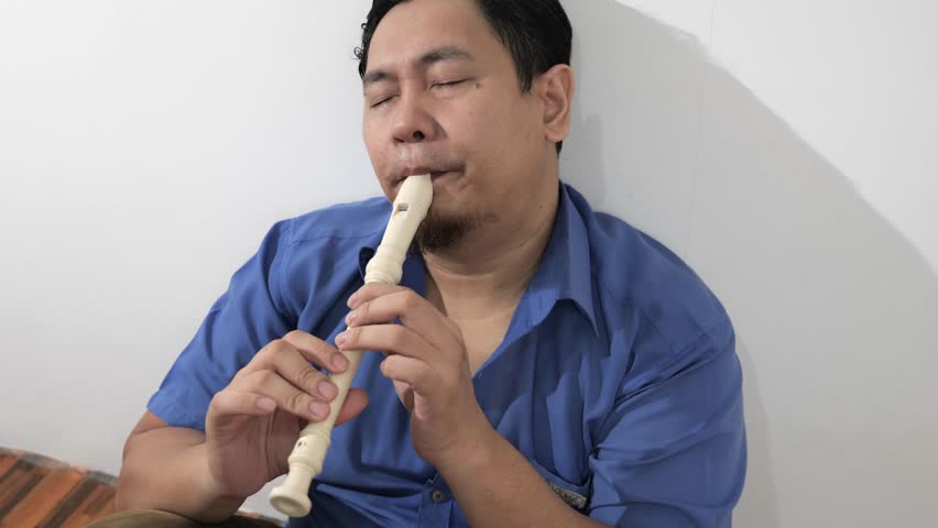 Young adult Asian man playing recorder flute, musical instrument