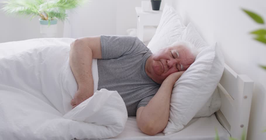 Senior man lying on side sleeping peacefully in soft comfortable bed with comfy pillow, tired elderly male, grandfather resting, falls asleep, taking nap in cozy bedroom, relaxation in retirement home