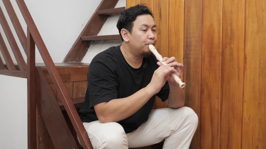Young adult Asian man playing recorder flute, musical instrument