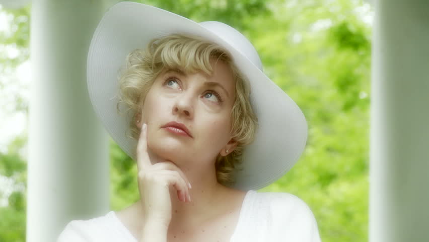 Close up of a cheerful blonde woman wearing a white hat and blouse. Pillars and