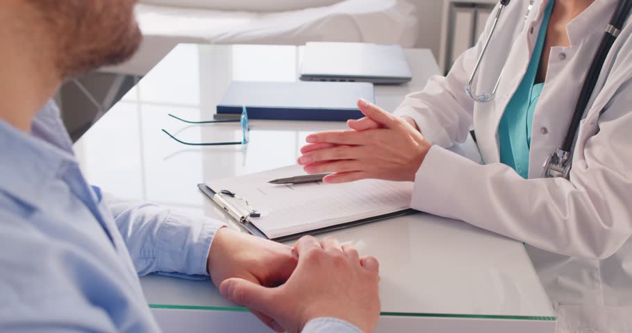 Female doctor in white uniform sitting at the desk in doctor's office making an appointment during examination in clinic. Man patient for medical checkup in hospital. 4k video. Slow motion video.