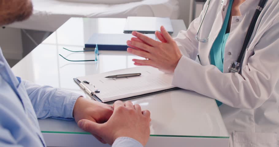 Female doctor in white uniform sitting at the desk in doctor's office making an appointment during examination in clinic. Man patient for medical checkup in hospital. 4k video. Slow motion video.
