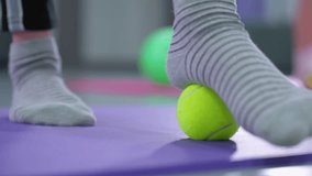 Close-up of person foot in socks rolling a yellow tennis ball underfoot on a purple mat, with a soft blur background and light reflection, focusing on foot therapy - Powered by Shutterstock - Get 15% off with code: PIKWIZARD15