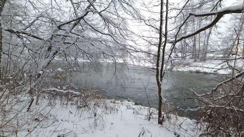 Snowfall over the thawed river. Winter landscape
