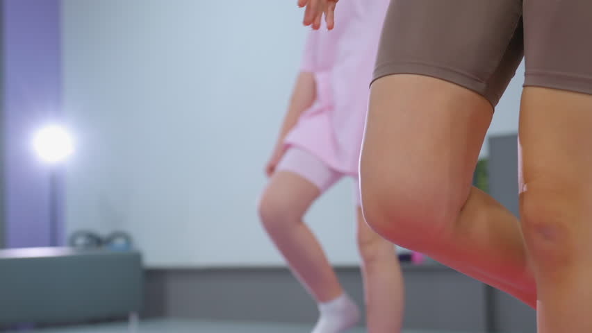 Close-up of children in a gym practicing balance on one leg, with a young girl in pink focusing intently on maintaining her stance amid a fitness session