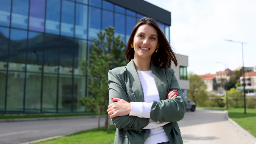 Young businesswoman smiling with folded arms in front of modern office building