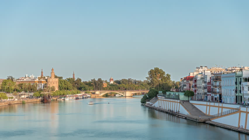 Aerial view of Seville split by Guadalquivir River timelapse hyperlapse. Triana district is known for flamenco, while Torre del Oro stands on other side. Waterfront and historic landmarks at sunset