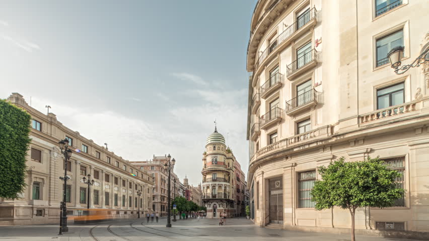 Pedestrians walking along Avda. de la Constitucion, major avenue in Casco Antiguo district of Seville, Spain. Timelapse hyperlapse with Edificio de la Adriatica, historical buildings and passing trams