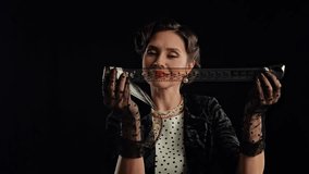 Professional model in studio. Retro woman actress with pin-up hairstyle and makeup isolated on black background, looks through long film reel tape, smiling positive expression. Slow motion. - Powered by Shutterstock - Get 15% off with code: PIKWIZARD15