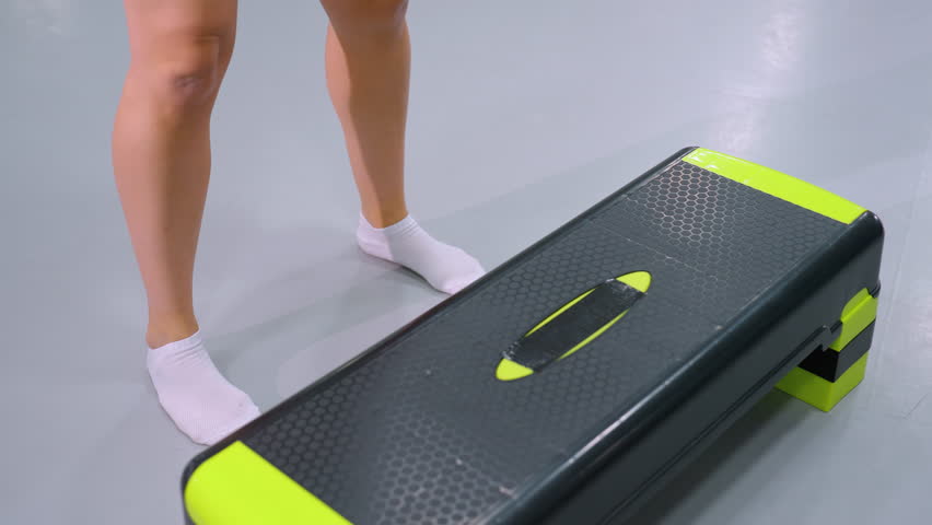 Close-up of person legs in white socks stepping onto and off workout bench during fitness routine, reflection on polished gym floor adds depth to dynamic movement and controlled step exercise
