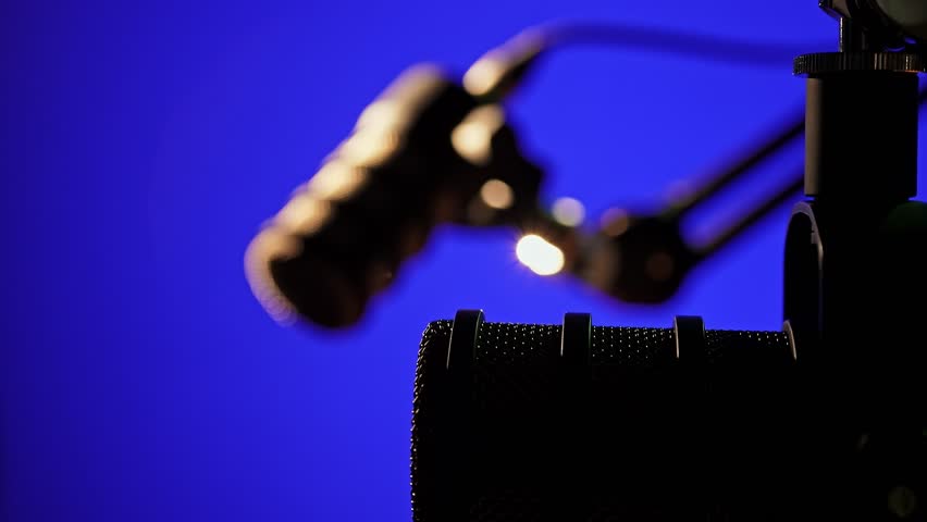 A high-quality dynamic microphone mounted on a boom arm, set against a blue-lit studio background. Ideal for podcasting, broadcasting, and professional voice recording.