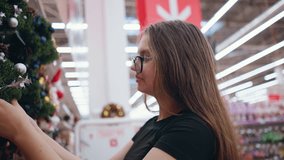 Shopper with well-manicured nails holding decorated Christmas wreath with silver ornaments, glittery holly leaves, and pinecones in holiday section of store filled with festive decorations - Powered by Shutterstock - Get 15% off with code: PIKWIZARD15