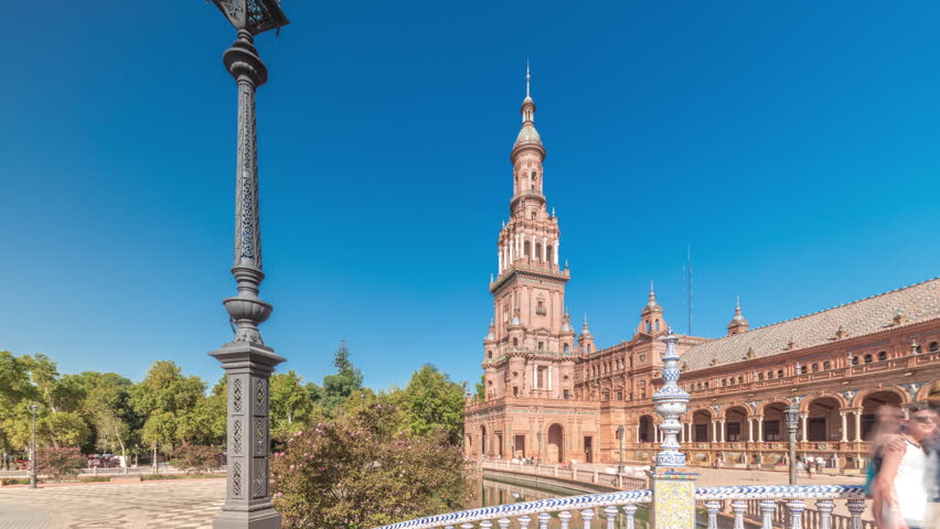 Panorama showing Plaza de Espana in Seville timelapse, a grand architectural complex in Maria Luisa Park built for the Ibero-American Exposition. Bridges, canal and vintage streetlights under blue sky