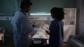 Doctor and nurse examine patient records near sleeping old patient. Medics focus on elderly man resting in bed connected to medical monitoring system - Powered by Shutterstock - Get 15% off with code: PIKWIZARD15