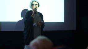 Elderly female speaker interacts with her audience during a presentation, holding a microphone and gesturing - Powered by Shutterstock - Get 15% off with code: PIKWIZARD15