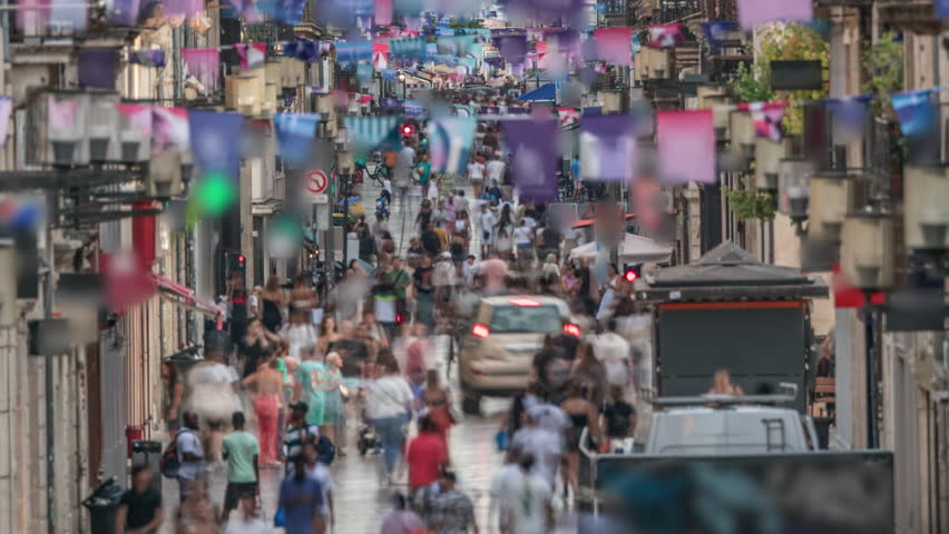 Tourists and locals walking and shopping in Rue Sainte-Catherine timelapse, Bordeaux, France. The longest pedestrian street in the country. Atmosphere of urban life. Colorful flags decorate the street