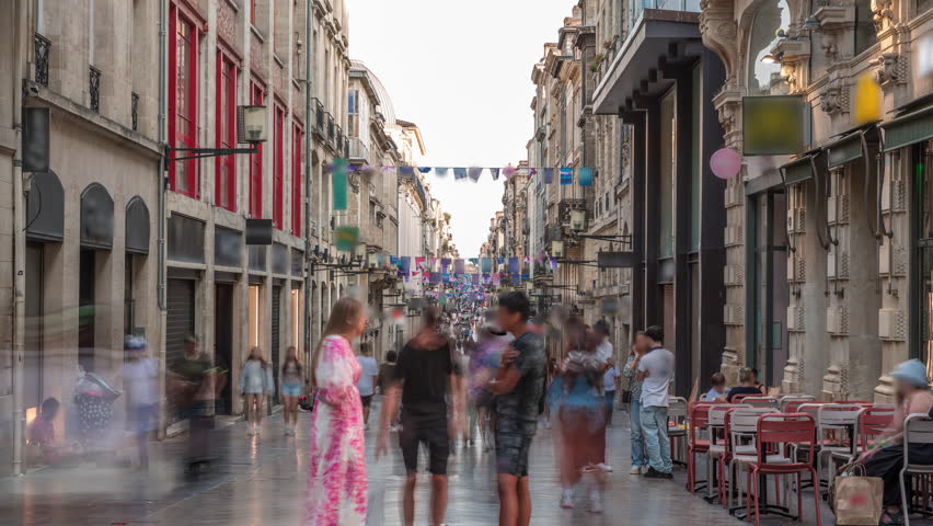 Tourists and locals walking and shopping in Rue Sainte-Catherine timelapse, Bordeaux, France. The longest pedestrian street in the country. Colorful flags decorate the street. Atmosphere of urban life
