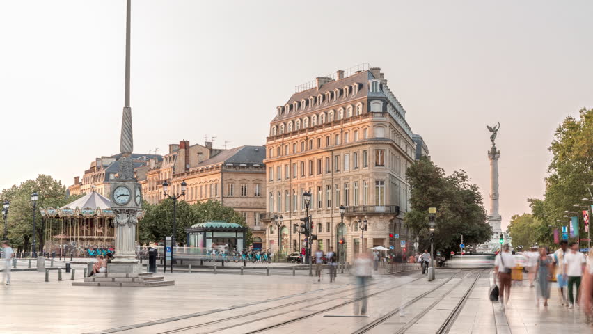 Triangular building and modern tram at Place de la Comedie timelapse, Bordeaux, France, during sunset. Shadow move across the facade and a streetlight with a clock adds elegance to this urban landmark