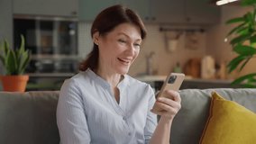 excited middle aged woman saying wow while looking at smartphone screen. happy moment of surprise and joy on cozy couch in stylish modern kitchen, natural light, real-life reactions at home - Powered by Shutterstock - Get 15% off with code: PIKWIZARD15