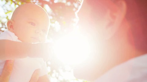 Loving young Caucasian father holding up happy baby son in sunshine outdoors sun lens flare shot on RED EPIC