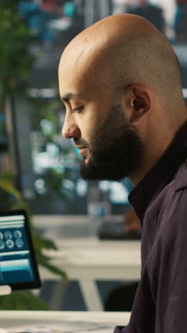 Vertical video Accountant in busy workplace talking with colleagues while inputting financial figures on PC. Employee working in modern office chatting with coworkers while crosschecking data, camera