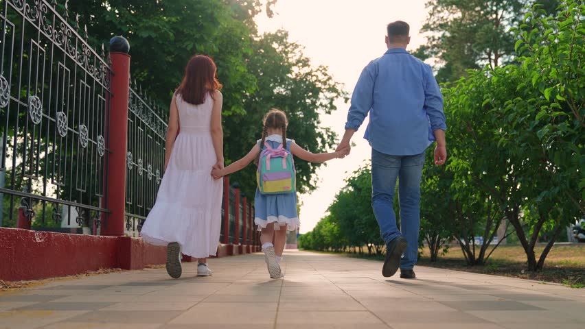 Mother father take child to school on street. Child daughter with backpacks, father mother go to school holding hands. Happy family. Girl child with parents go to school. Concept of children education