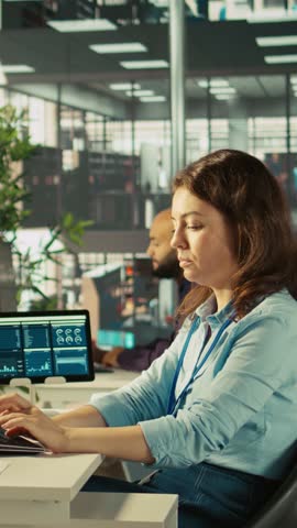 Vertical video Woman suffering from migraine at work, reading medication prescription. Employee experiencing headache while reviewing financial charts on computer monitor at office desk, camera B