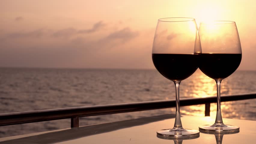 Glasses with red wine and sunset with sea background. Romantic luxury evening on cruise yacht with winery setting