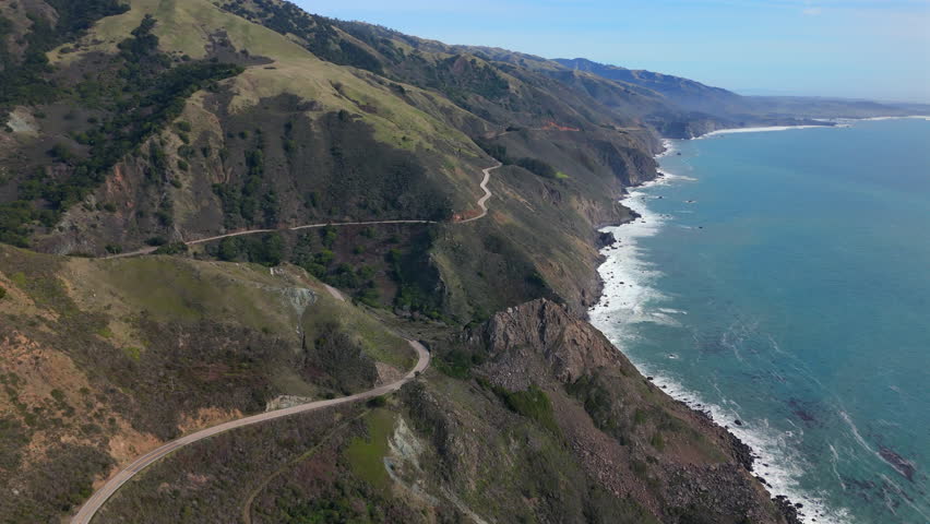 This aerial view of Big Sur shows Highway 1 winding along Californias coastline, with a single car amid majestic mountains and beautiful natural landscapes by the captivating ocean