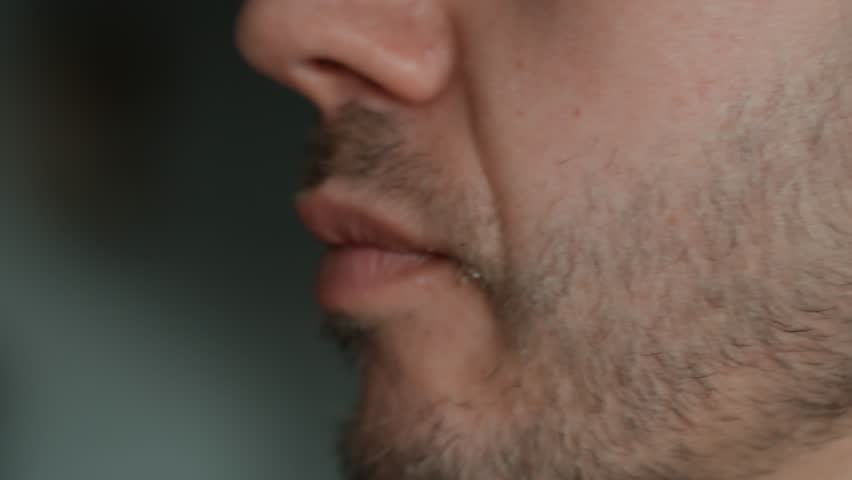Close up of mouth takes big bite of seeded bagel filled with egg, cheese, tomato and greens. Hungry man eats sandwich