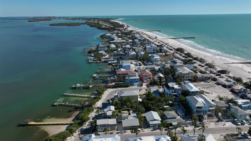 Beautiful city of Bradenton in Florida at sunlight. Clear water of bay with jetty and piers. Traffic on main street and resting people on white sandy beach. Reaching waves of sea. Aerial wide shot.