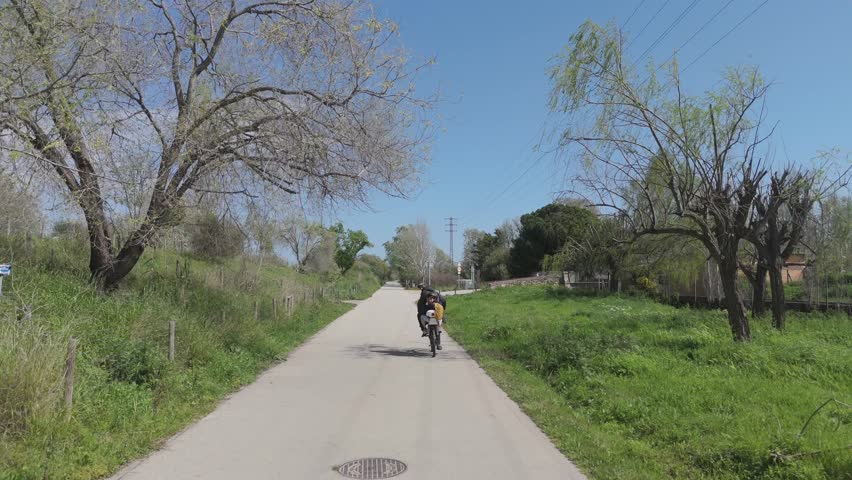  Cyclist pedals down a quiet country road under a blue sky. Aerial view of a peaceful bike ride in nature.