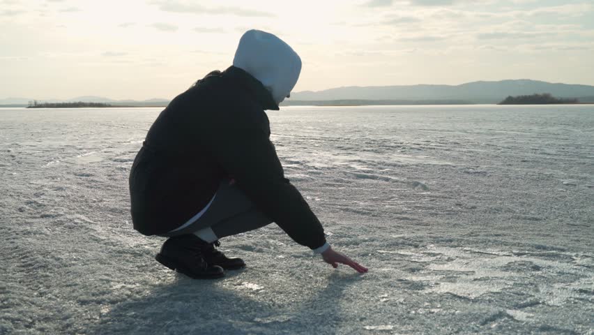 A young woman gently touches the melting spring ice on the lake. Icy surface, sensual touch. The texture of ice.