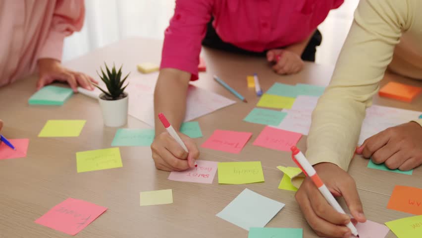 Slow motion hand closeup of startup employee team brainstorming strategic marketing plan and making mind map with colorful sticky notes placed on office table at meeting room. Variegated
