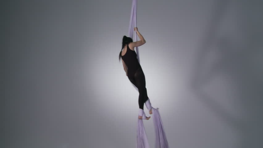 Athletic young woman does splits while doing aerial yoga. Wide shot with a small