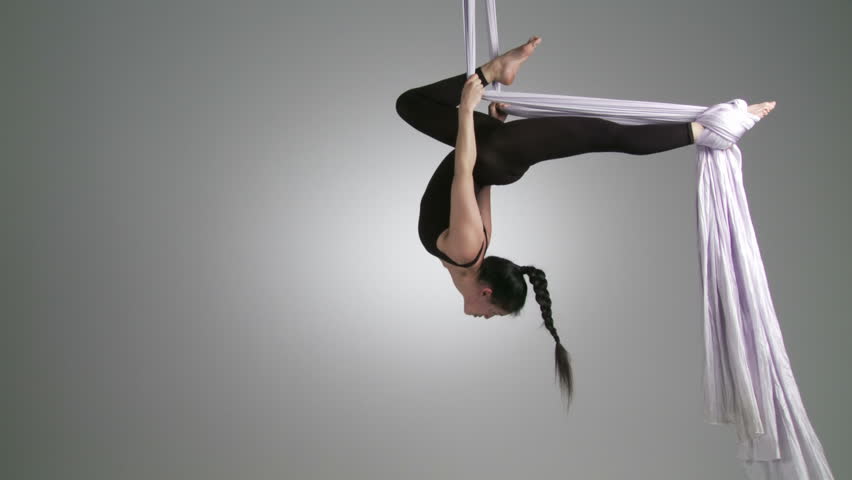 Gymnastic young woman holds an inverted position while doing aerial yoga. Wide