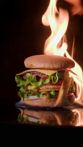Beef burger on fire rotating on black background close up, vertical video