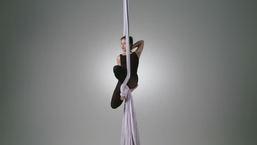 Gymnastic young woman in sitting positions while doing aerial yoga. Wide shot
