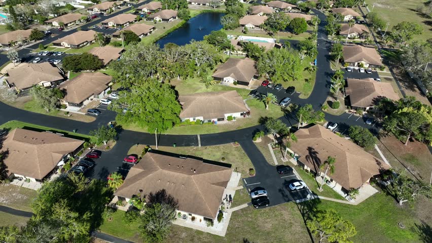 Large Villas Homes with property during sunny day. Aerial approaching shot. Lake in center with swimming pool. Parking cars driveway. Expensive and noble residential area of Bradenton, Florida, USA.